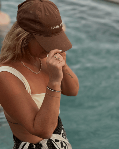 Woman wearing Golden Hour Cap Society Dad Cap in a pool with gold jewellery Australia