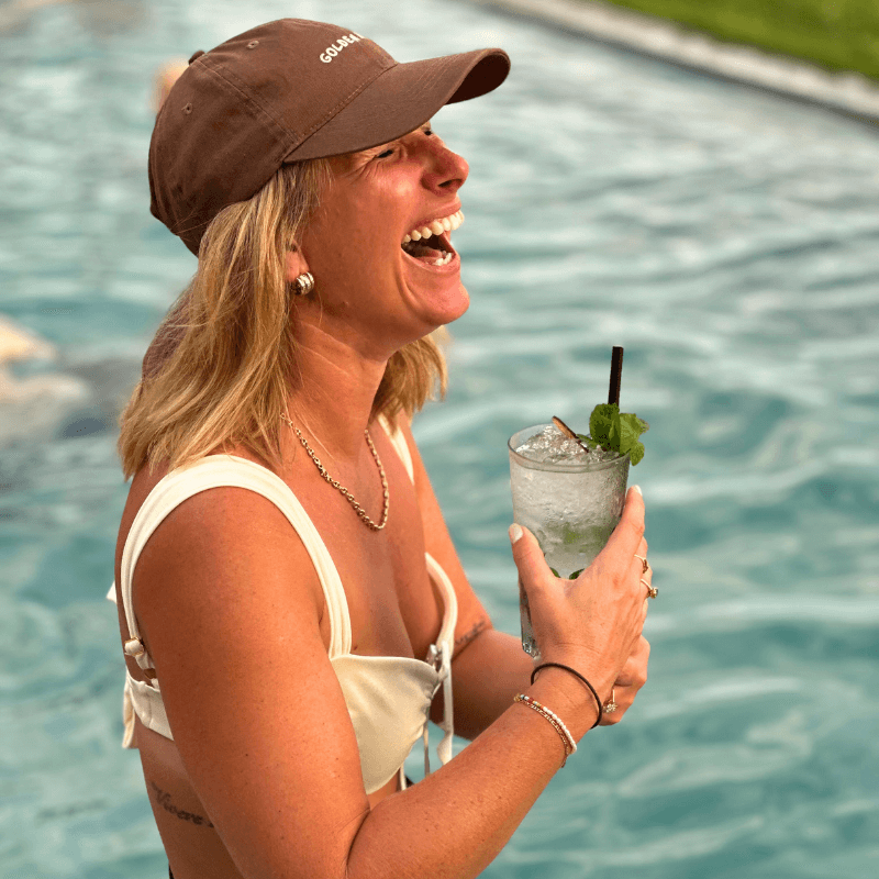 Woman holding a cocktail poolside wearing brown mid-profile cap in brown with Golden Hour embroidery