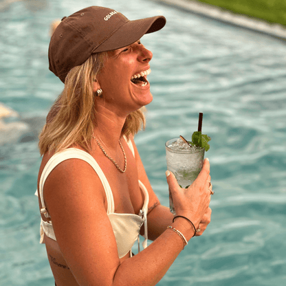 Woman holding a cocktail poolside wearing brown mid-profile cap in brown with Golden Hour embroidery